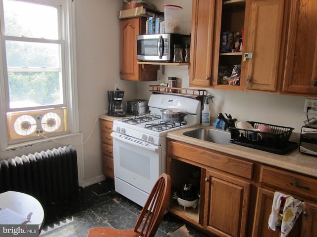 kitchen featuring white gas stove, dark tile floors, radiator heating unit, and sink