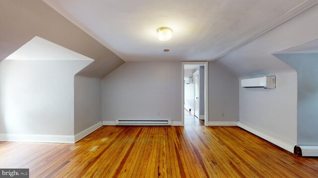 additional living space with baseboard heating, lofted ceiling, light hardwood / wood-style flooring, and a wall mounted AC