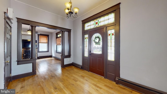 entryway featuring a notable chandelier, baseboard heating, decorative columns, and light wood-type flooring