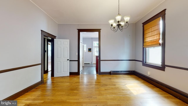 empty room with crown molding, light hardwood / wood-style floors, a baseboard radiator, and an inviting chandelier