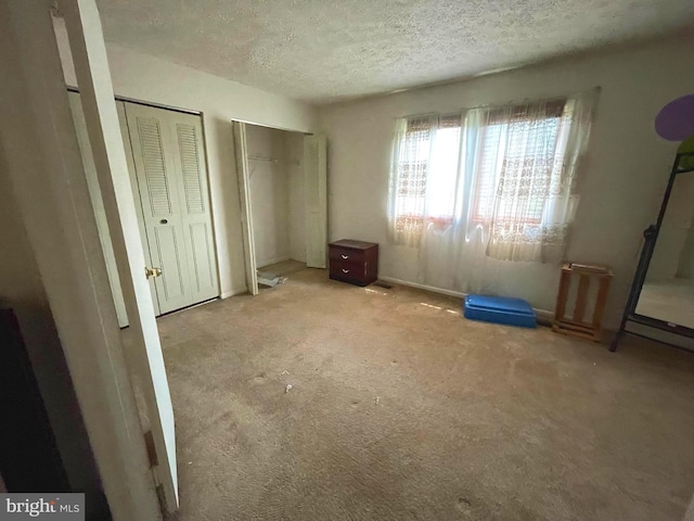 unfurnished bedroom featuring a textured ceiling, carpet floors, and two closets