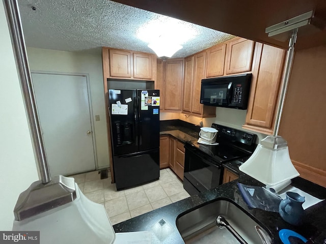 kitchen with a textured ceiling, light tile patterned flooring, a sink, dark stone counters, and black appliances