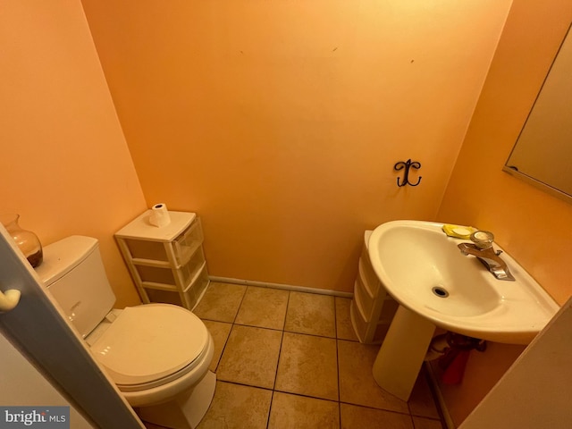 half bath with tile patterned flooring, baseboards, a sink, and toilet