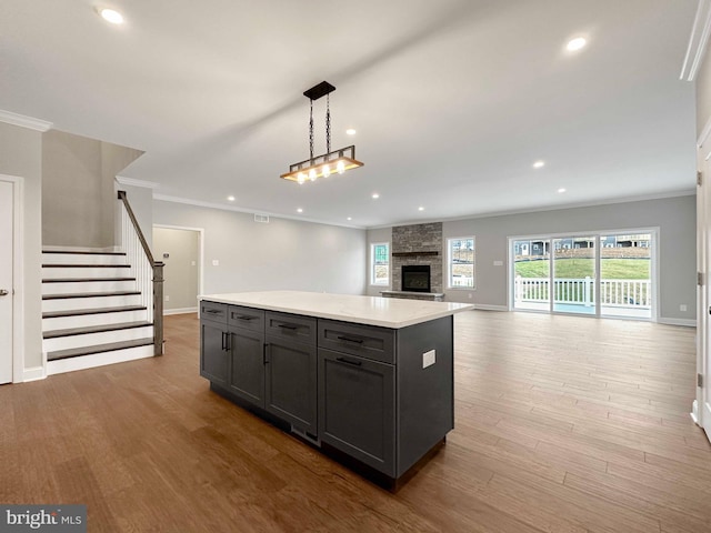 kitchen with a center island, decorative light fixtures, ornamental molding, a stone fireplace, and light hardwood / wood-style flooring