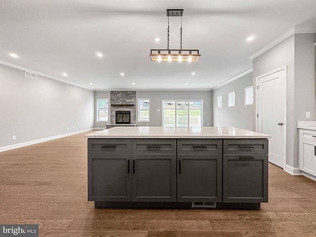 kitchen with ornamental molding, a stone fireplace, hardwood / wood-style flooring, and pendant lighting