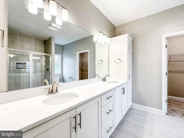 bathroom featuring toilet, vanity with extensive cabinet space, a shower with door, dual sinks, and tile flooring