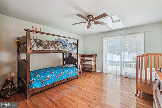 bedroom featuring a skylight, access to exterior, ceiling fan, and light wood-type flooring