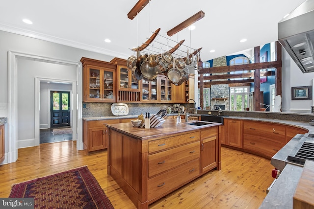 kitchen with a center island with sink, backsplash, light wood-type flooring, and hanging light fixtures