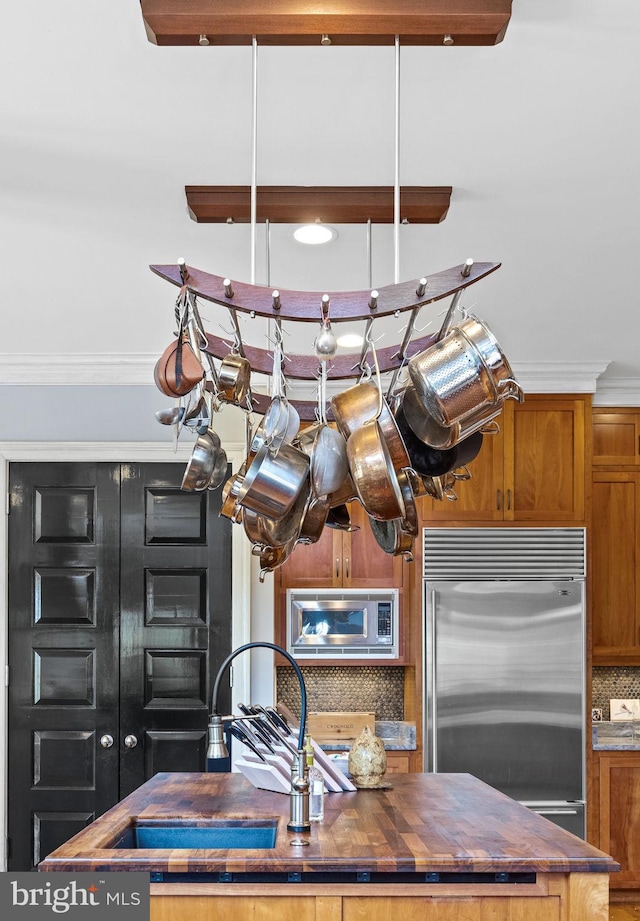 kitchen featuring wood counters, backsplash, crown molding, sink, and built in appliances