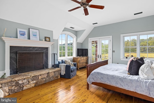 bedroom featuring french doors, a stone fireplace, vaulted ceiling, ceiling fan, and light wood-type flooring