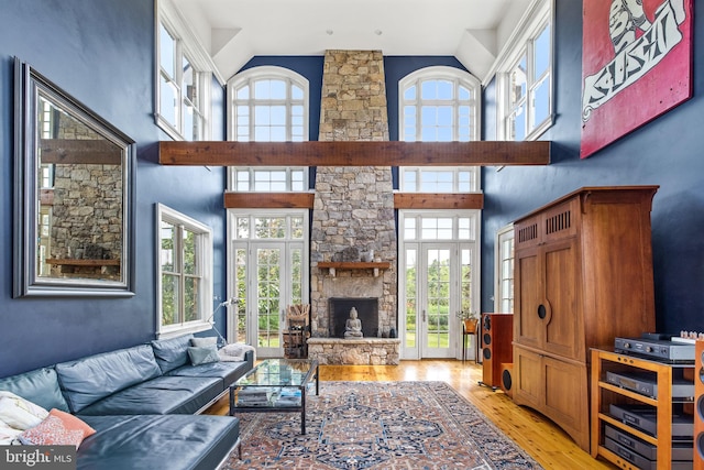 living room with a stone fireplace, french doors, a towering ceiling, and light wood-type flooring