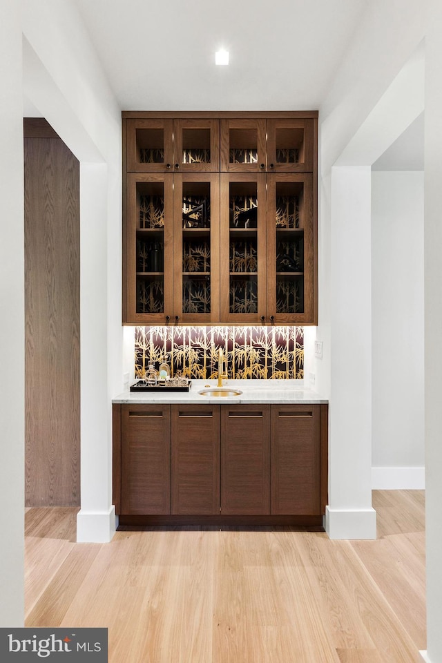 bar featuring backsplash, sink, dark brown cabinetry, and light wood-type flooring