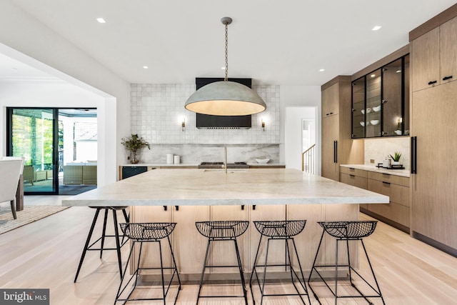 kitchen with light hardwood / wood-style floors, decorative light fixtures, backsplash, and a kitchen breakfast bar