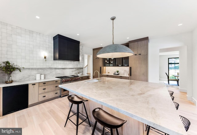 kitchen featuring an island with sink, a breakfast bar area, light wood-type flooring, pendant lighting, and stainless steel range