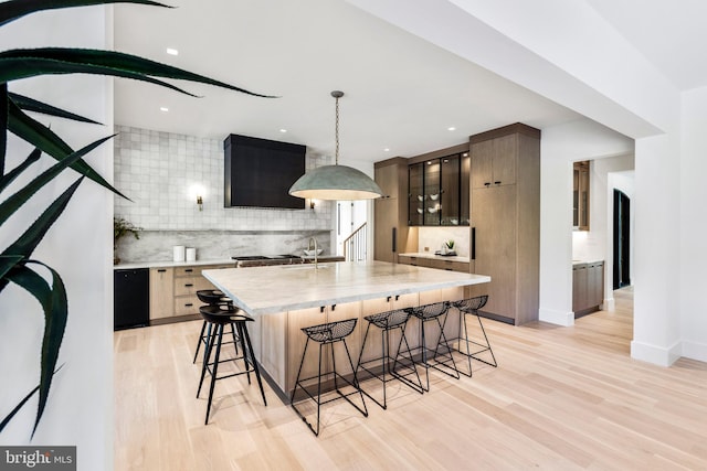 kitchen with light hardwood / wood-style floors, hanging light fixtures, backsplash, and an island with sink