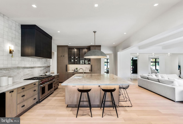 kitchen with a kitchen island with sink, a kitchen breakfast bar, hanging light fixtures, range with two ovens, and sink