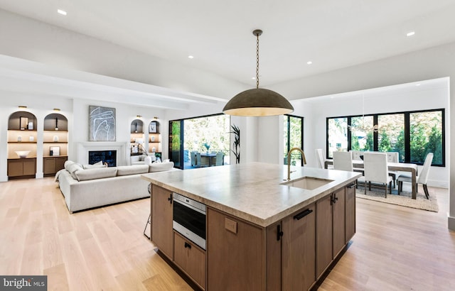 kitchen with sink, an island with sink, light hardwood / wood-style flooring, and decorative light fixtures