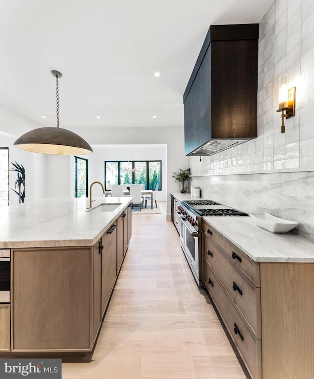 kitchen featuring wall chimney range hood, hanging light fixtures, light stone countertops, range with two ovens, and sink