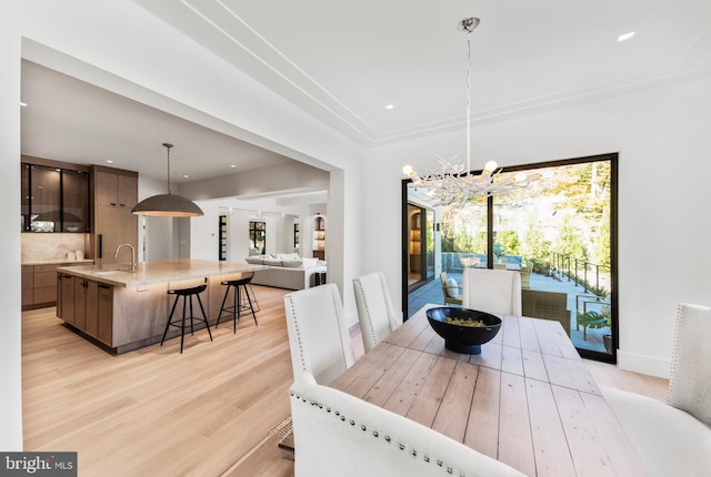 dining space featuring sink, light hardwood / wood-style flooring, and an inviting chandelier