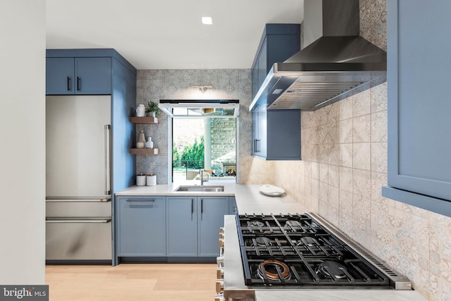 kitchen with high end refrigerator, wall chimney exhaust hood, sink, and backsplash