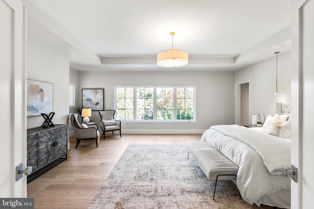 bedroom with a tray ceiling and light wood-type flooring