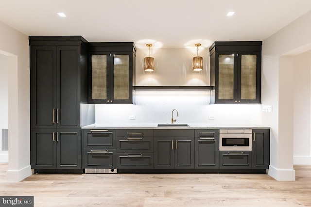 bar featuring stainless steel microwave, sink, hanging light fixtures, and light wood-type flooring