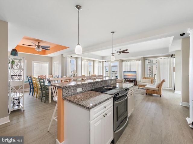 kitchen featuring ceiling fan, electric range, white cabinets, light hardwood / wood-style floors, and a tray ceiling