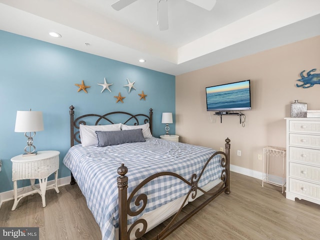 bedroom featuring a raised ceiling, ceiling fan, and light wood-type flooring