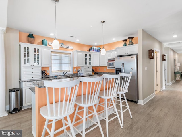 kitchen featuring a kitchen breakfast bar, light wood-type flooring, decorative light fixtures, stainless steel refrigerator with ice dispenser, and a center island