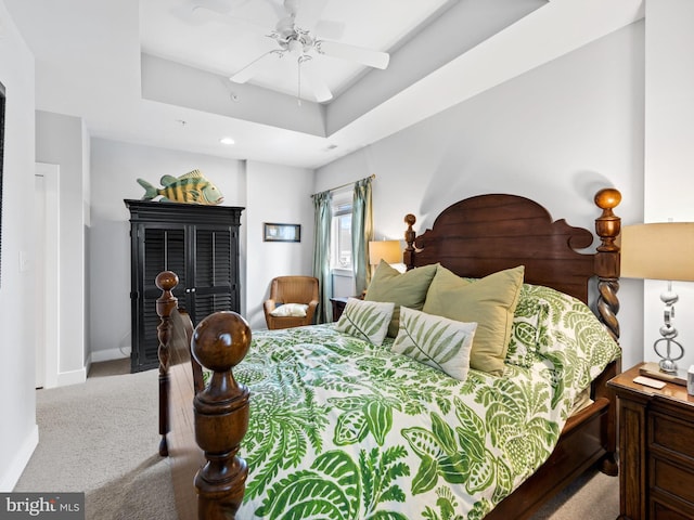 carpeted bedroom with ceiling fan and a tray ceiling