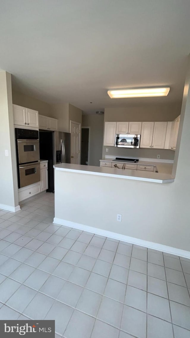 kitchen with appliances with stainless steel finishes, white cabinetry, and light tile floors