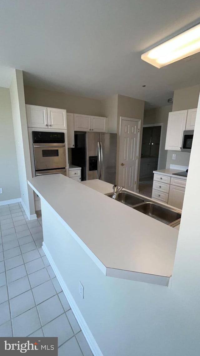 kitchen with appliances with stainless steel finishes, sink, light tile floors, and white cabinets