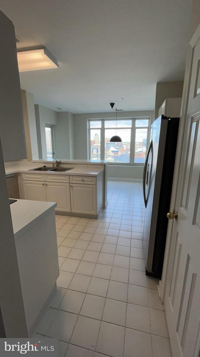 kitchen featuring light tile flooring, sink, white cabinets, stainless steel refrigerator, and pendant lighting