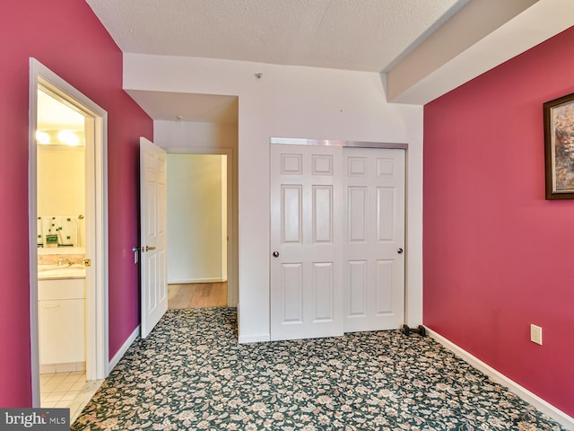 unfurnished bedroom featuring connected bathroom, light tile floors, a textured ceiling, a closet, and sink