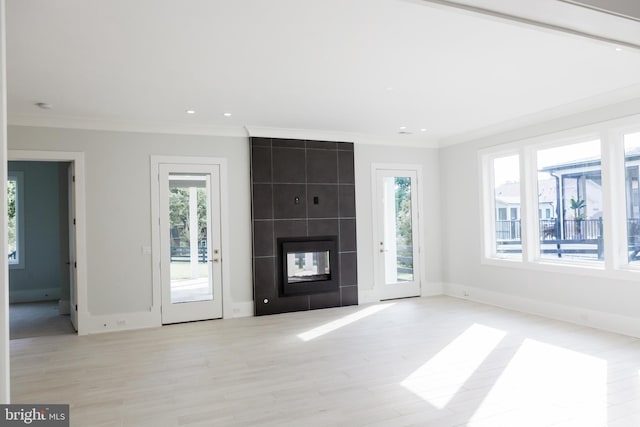 unfurnished living room featuring light hardwood / wood-style floors, a tile fireplace, a healthy amount of sunlight, and tile walls