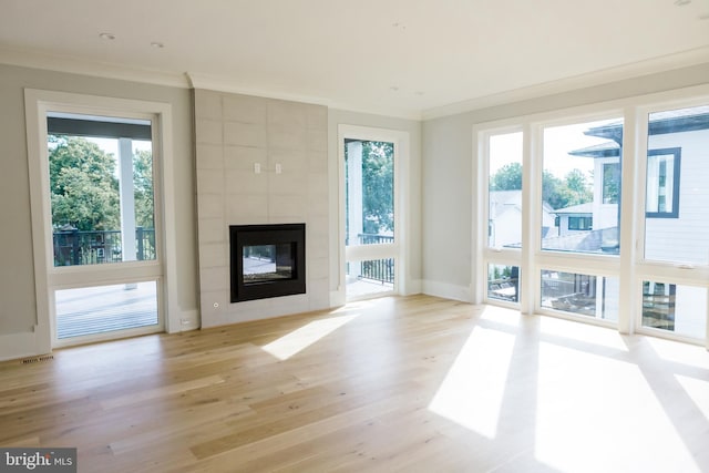 unfurnished living room with light hardwood / wood-style flooring, tile walls, ornamental molding, and a tiled fireplace