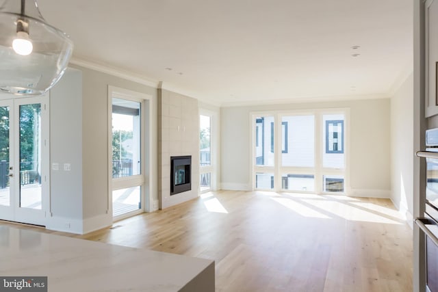 unfurnished living room with crown molding, a tiled fireplace, and light hardwood / wood-style floors