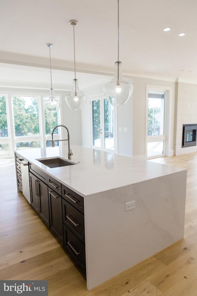 kitchen with an island with sink, light hardwood / wood-style floors, dishwashing machine, hanging light fixtures, and sink