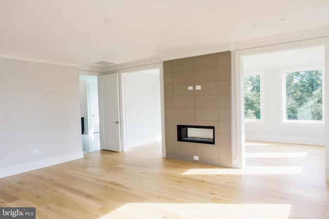 unfurnished living room with a tile fireplace, tile walls, light hardwood / wood-style floors, and crown molding