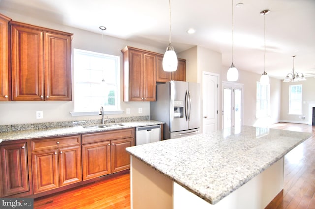 kitchen featuring an inviting chandelier, light stone counters, light hardwood / wood-style floors, pendant lighting, and sink