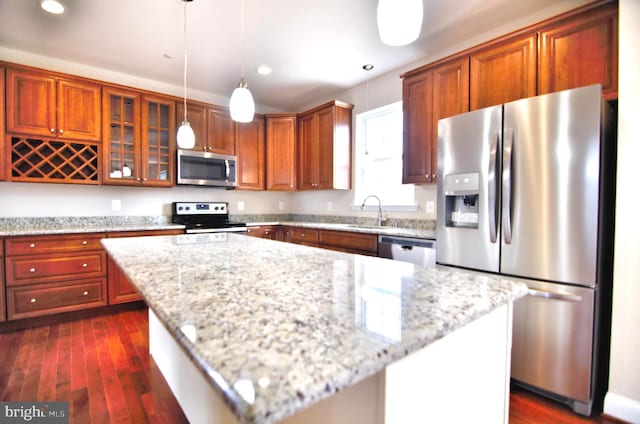 kitchen with dark hardwood / wood-style flooring, pendant lighting, stainless steel appliances, a center island, and light stone countertops