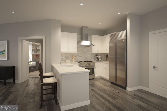 kitchen featuring kitchen peninsula, wall chimney exhaust hood, premium appliances, sink, and white cabinets