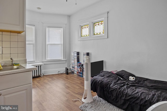 bedroom featuring radiator heating unit, sink, and light hardwood / wood-style flooring