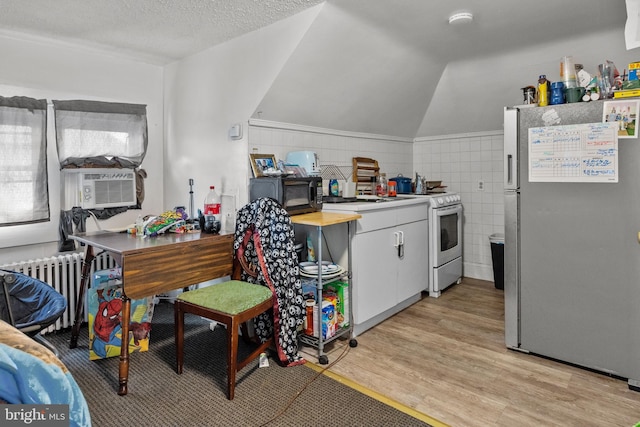 kitchen featuring tile walls, light wood-type flooring, stainless steel fridge, lofted ceiling, and electric stove