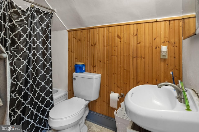 bathroom with toilet, wooden walls, lofted ceiling, tile floors, and sink