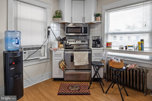 kitchen with white cabinets, radiator, light hardwood / wood-style flooring, backsplash, and stainless steel appliances