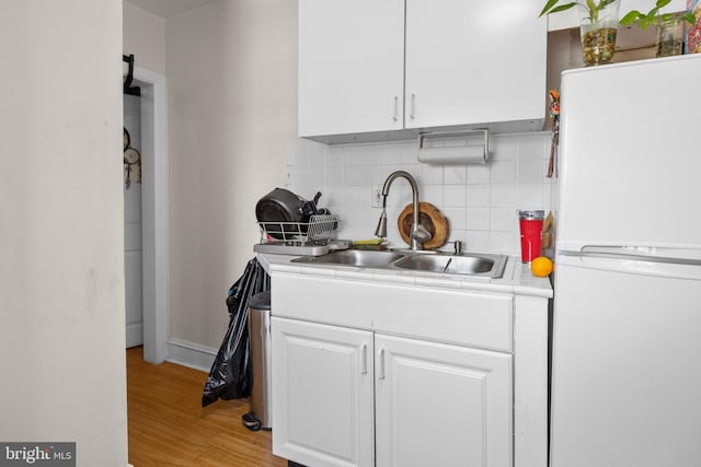 kitchen with sink, white fridge, white cabinets, light hardwood / wood-style flooring, and backsplash