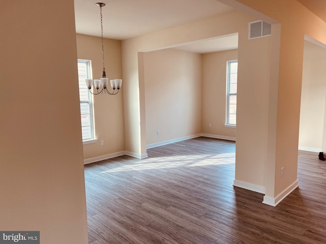 empty room with dark hardwood / wood-style flooring, a notable chandelier, and a healthy amount of sunlight