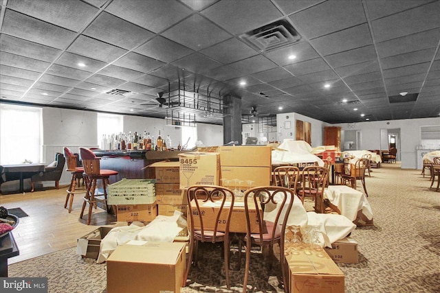 carpeted dining area with bar, ceiling fan, and a drop ceiling