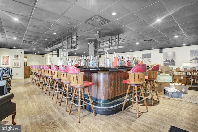 bar with light hardwood / wood-style floors and a drop ceiling